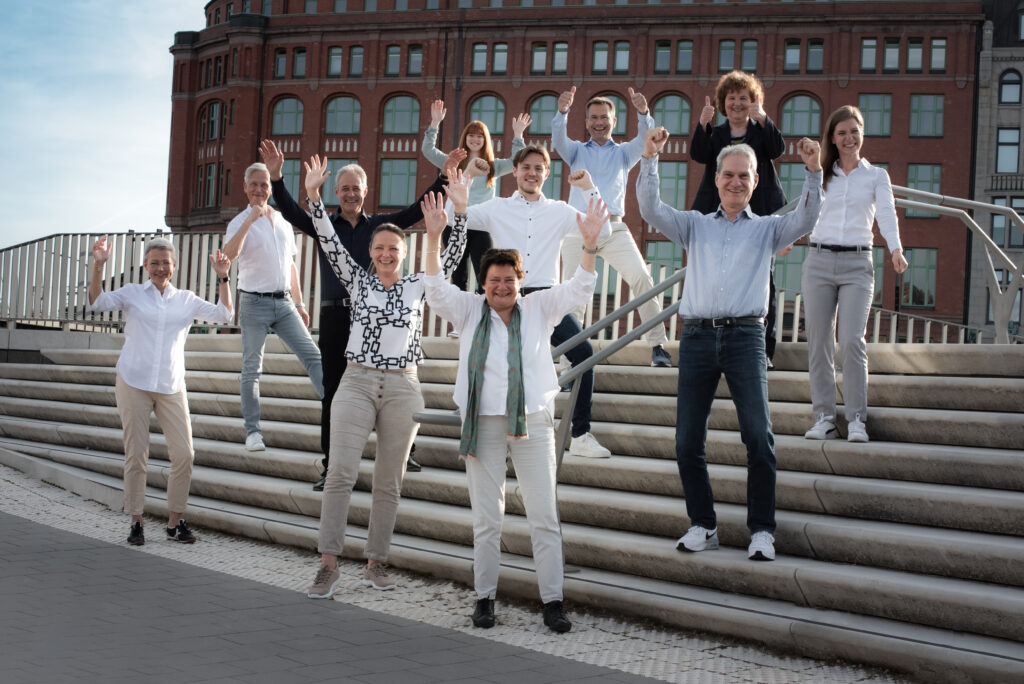 Das gesamte Team von relations Hamburg mit hoch erhobenen Armen auf einer Treppe in der Speicherstadt