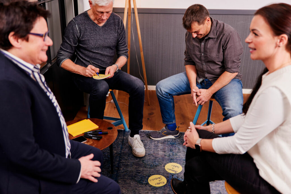 Vier Mitarbeiter von relations Hamburg sitzen auf Hockern bei einem Workshop, schreiben auf Karteikarten und reden miteinander