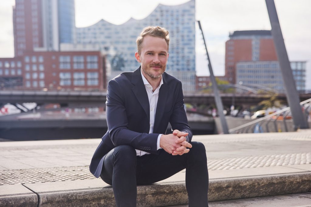Timm Schröder sitzt auf Treppe vor Geschäftssitz am Hamburger Hafen