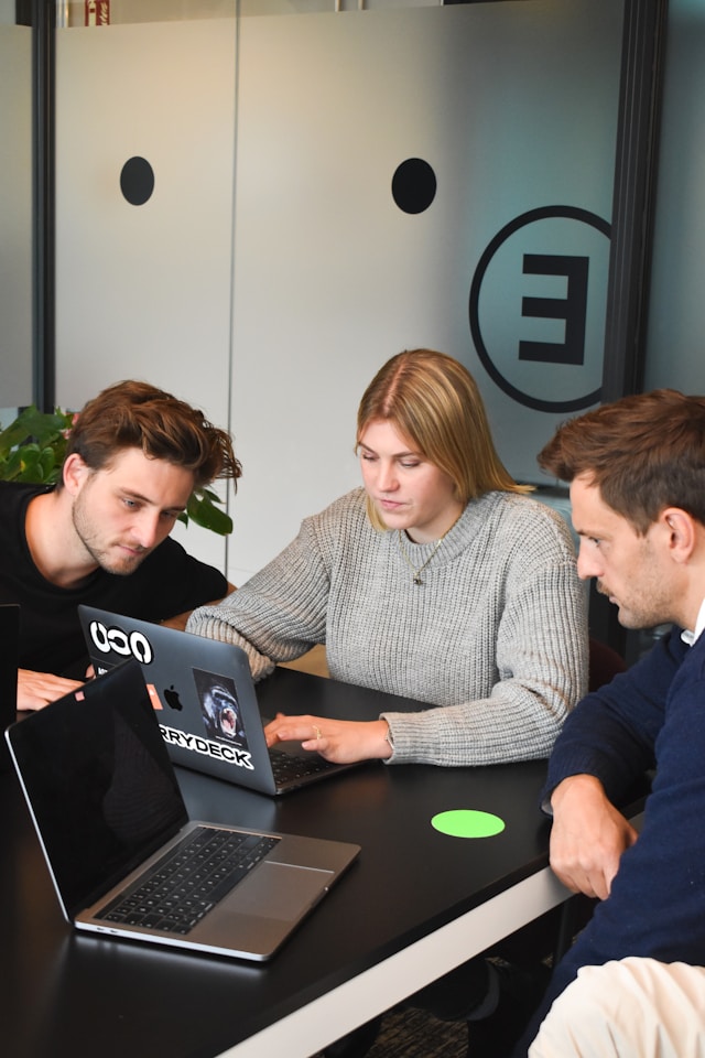 3 Kolleg:innen sitzen konzentriert aussehend vor einem Notebook