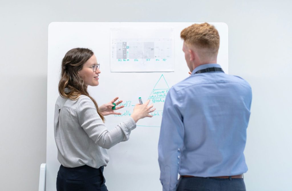 Zwei Teamkolleg:innen besprechen sich vor einem Whiteboard.